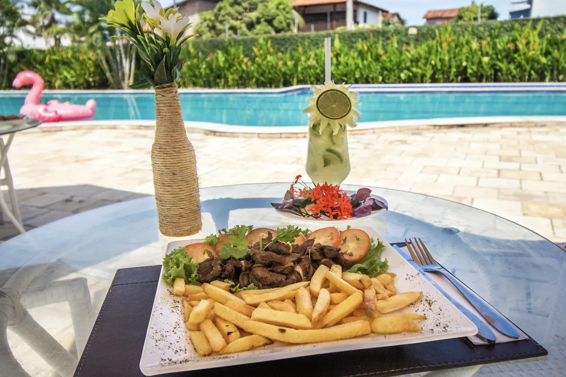 Um prato de comida e uma bebida sobre uma mesa em frente a uma piscina.