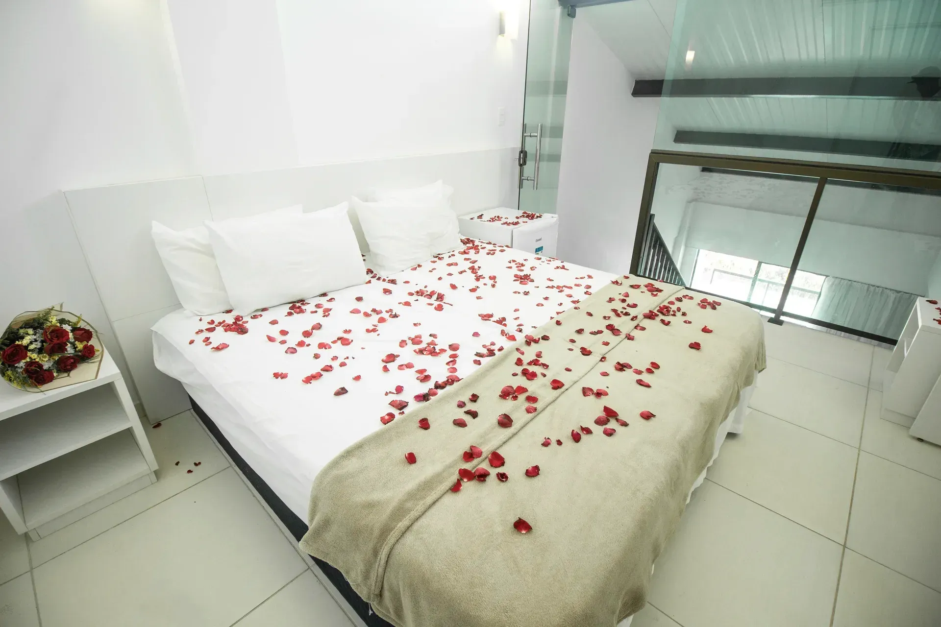 Uma cama com pétalas de rosa vermelhas em um quarto de hotel.