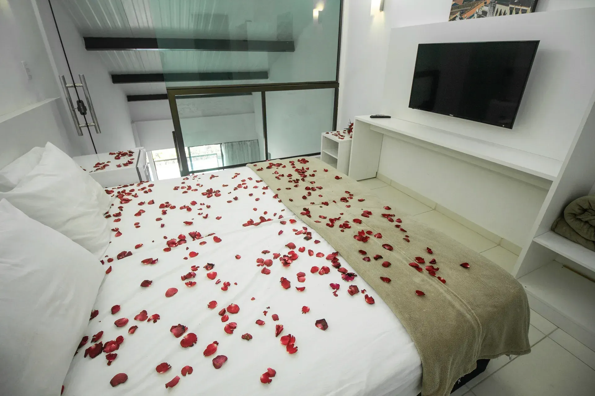 Um quarto com cama coberta de pétalas de rosa e TV de tela plana.