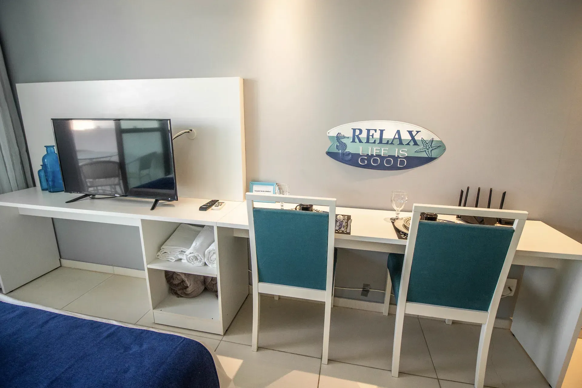 Um quarto com cama, mesa, cadeiras e televisão.