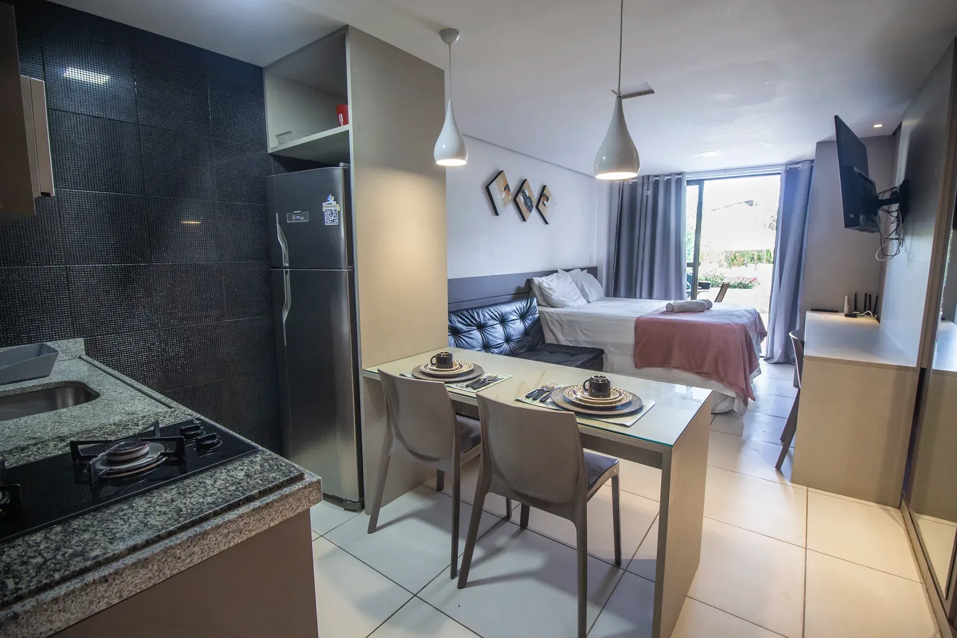 Um pequeno apartamento com mesa e cadeiras e geladeira.