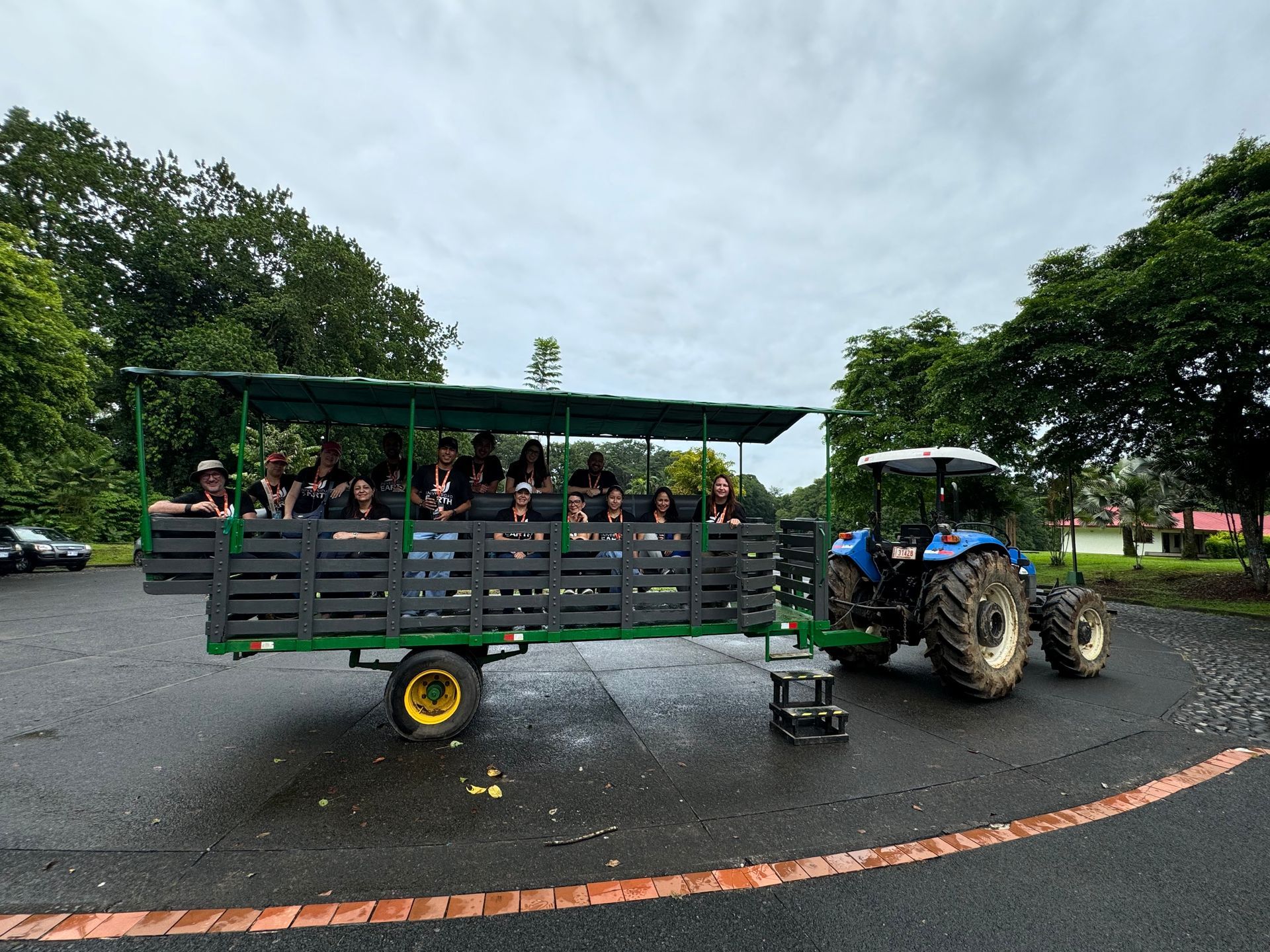 Un tractor tira de un vagón lleno de gente, al aire libre. El vagón tiene un marco verde y la gente mira hacia adelante.