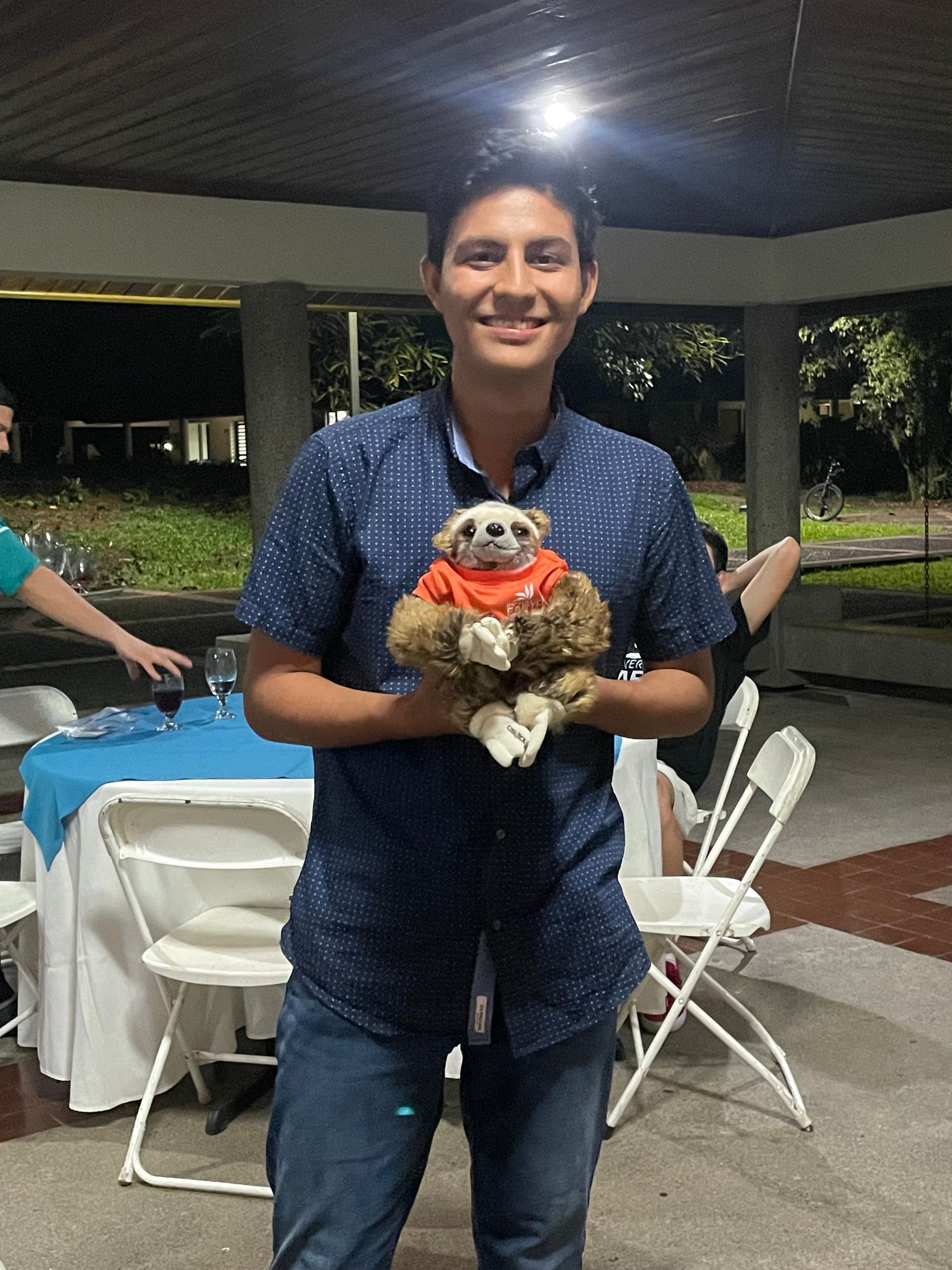 A man in a blue shirt is holding a stuffed sloth