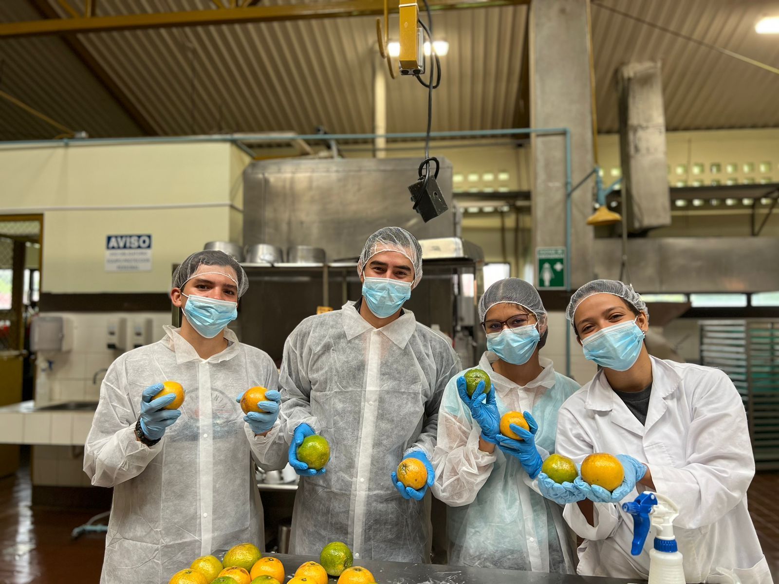 A group of people wearing masks are holding oranges in a kitchen.
