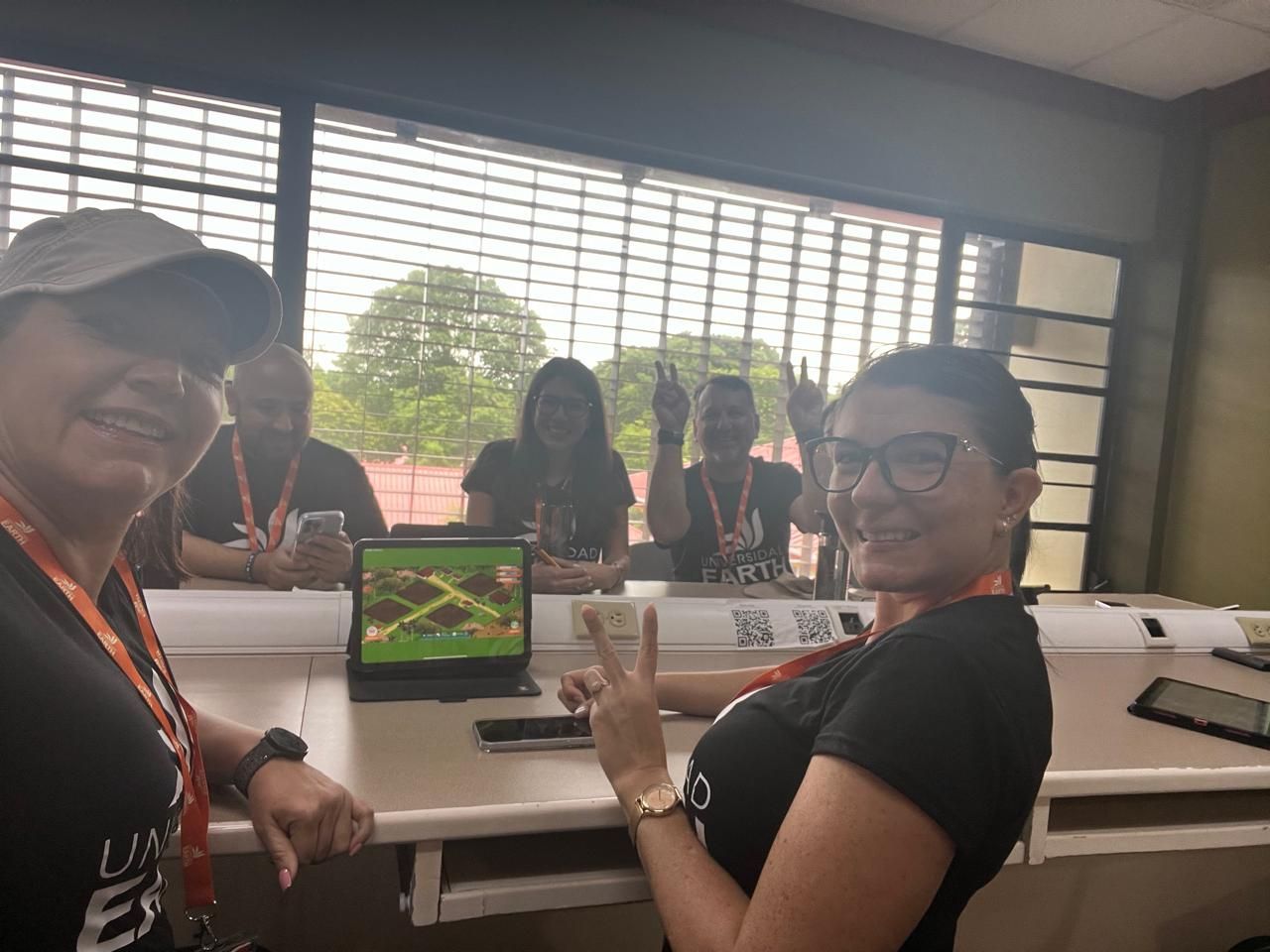 Grupo de mujeres sonriendo, en una sala con tecnología, una de ellas haciendo el signo de la paz.