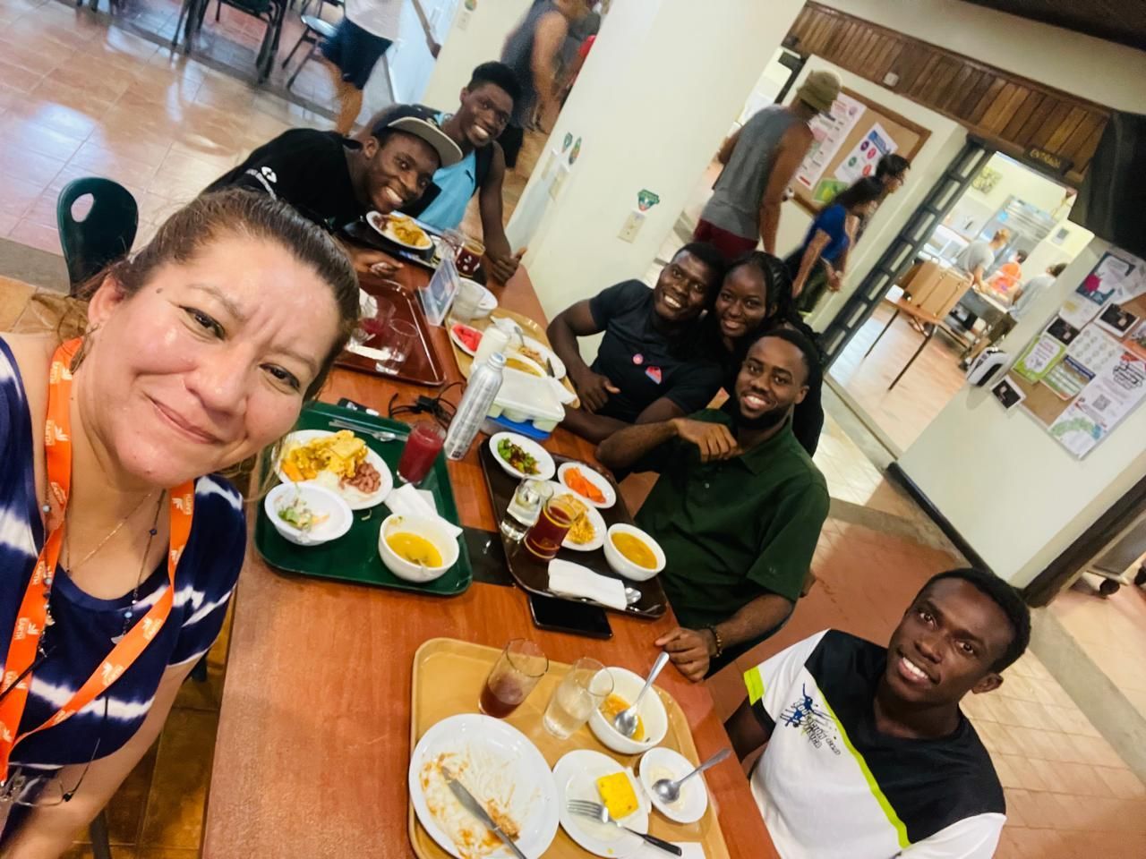 Un grupo de personas sonriendo en una mesa de una cafetería, comiendo.