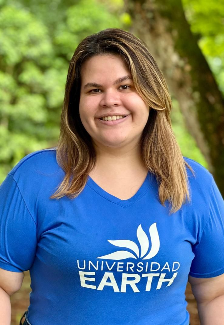 Mujer sonriente de cabello oscuro con camiseta negra sin mangas y collar. Al fondo se ven una puerta y una obra de arte colorida.