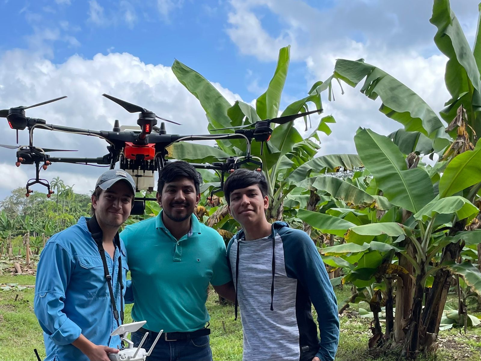 Three men are posing for a picture with a drone in the background.