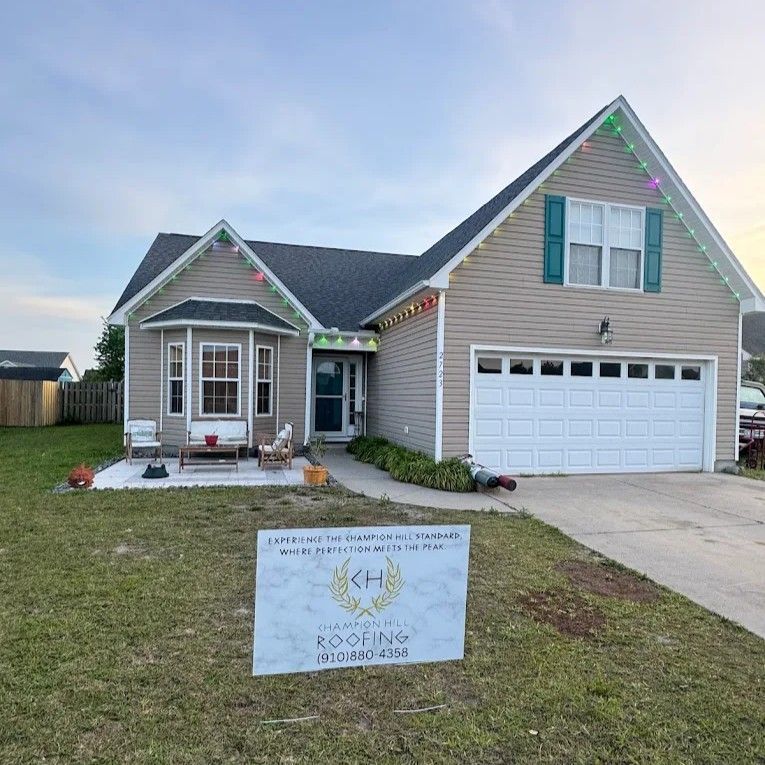 House with siding, garage, green shutters, and a roofing sign in the yard.