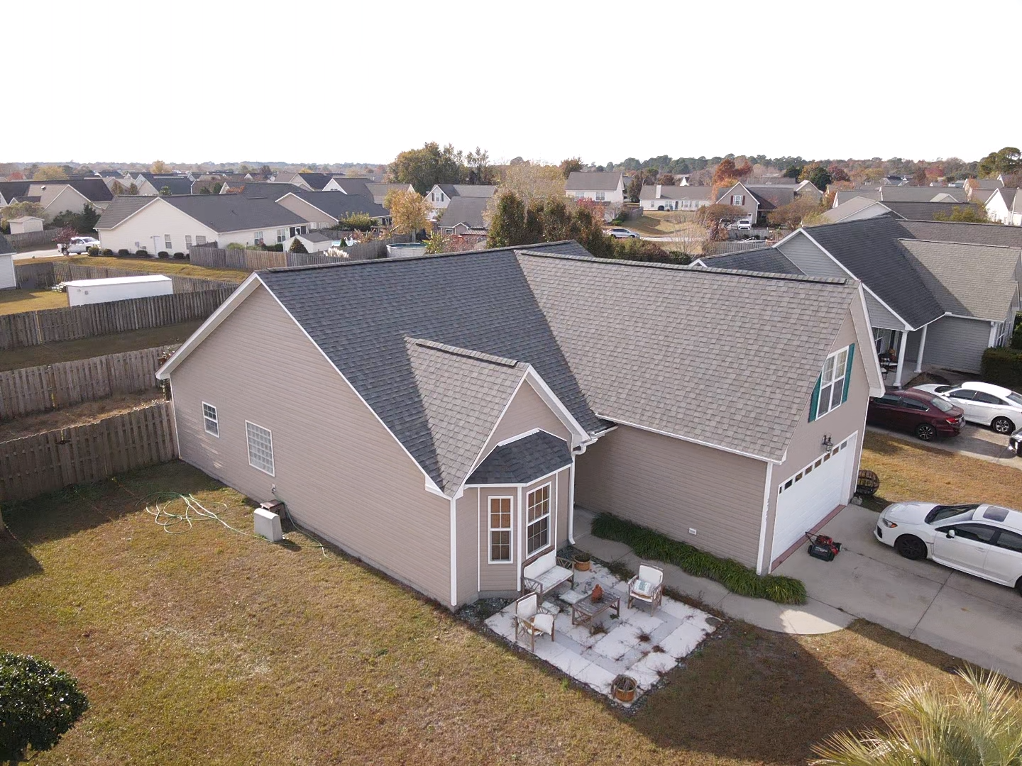 An aerial view of a tan house with a dark gray roof in a suburban neighborhood.