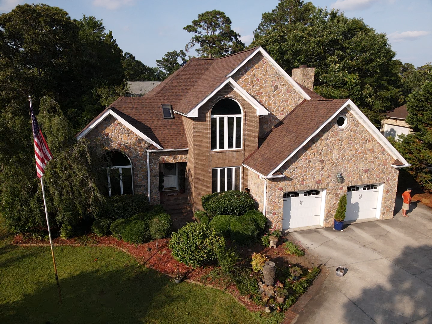Two-story brick house with brown roof and two-car garage; American flag in front yard.