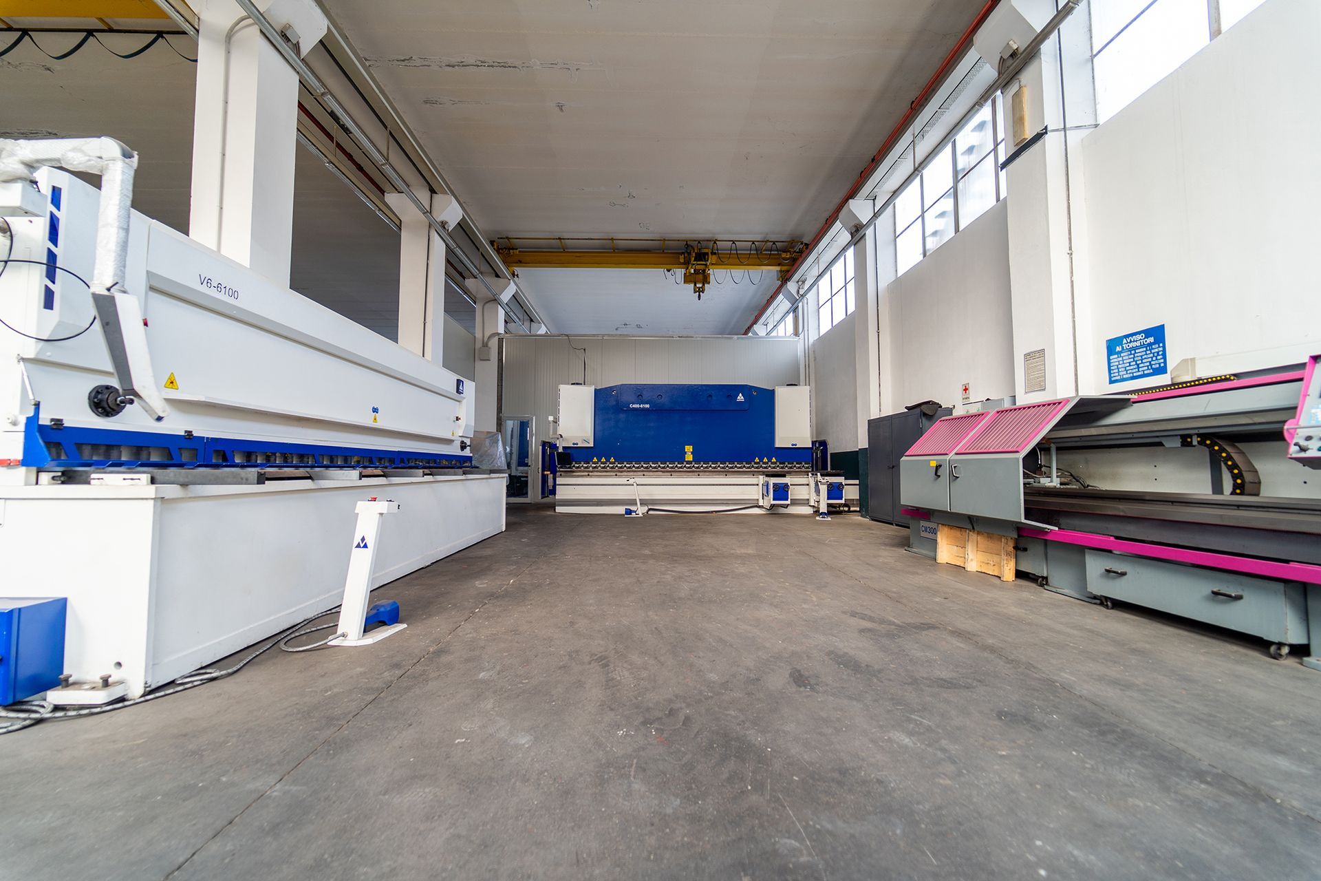 Interno di una fabbrica metallurgica con grandi macchinari bianchi e blu e una gru a ponte gialla.