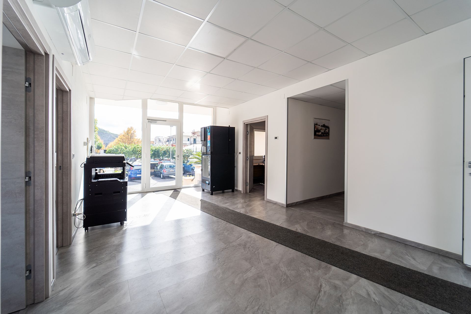 Corridoio luminoso dell'ufficio con ampie finestre, pavimenti grigi e pareti bianche.