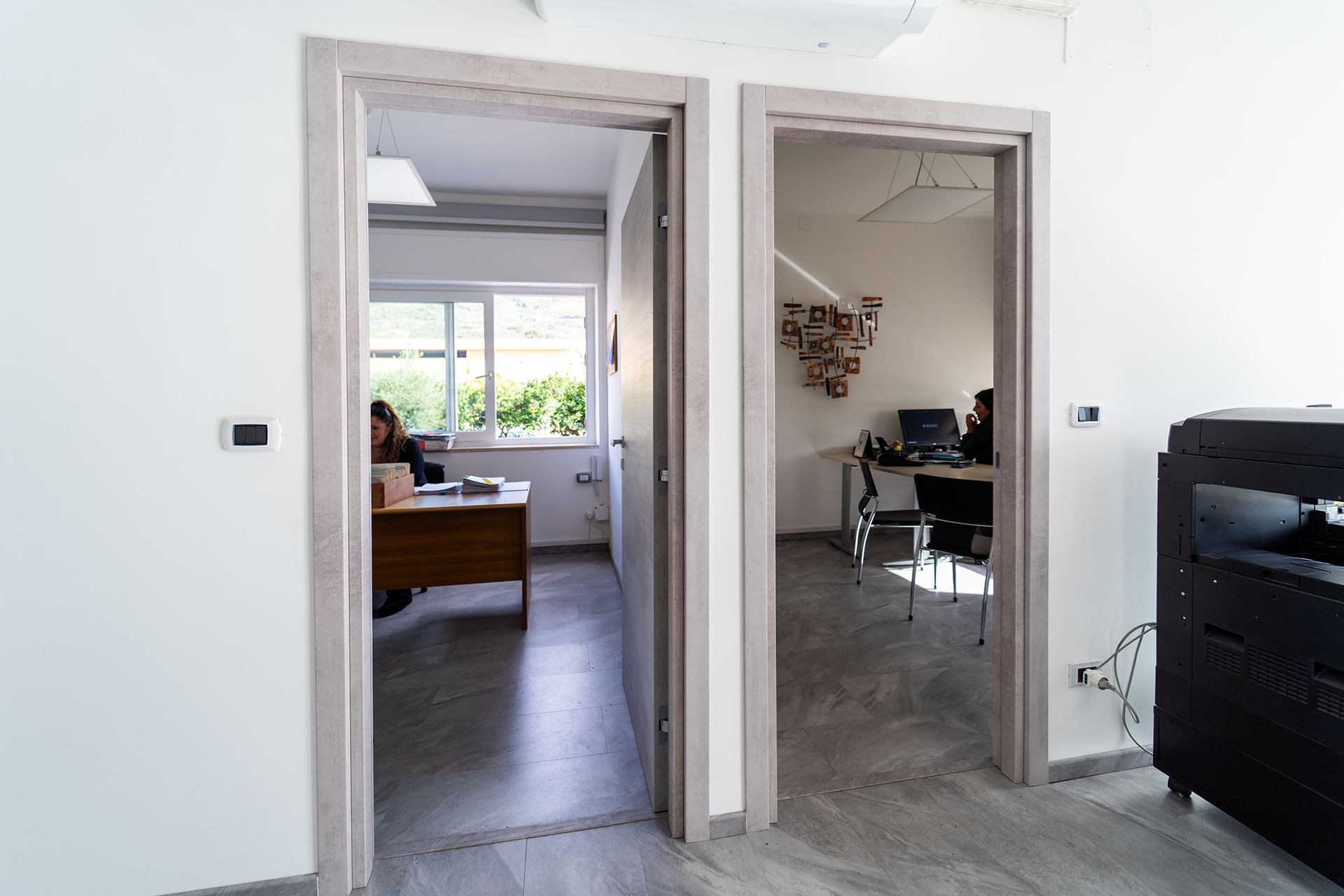 Due porte aperte che danno su uffici con dipendenti seduti alle scrivanie.