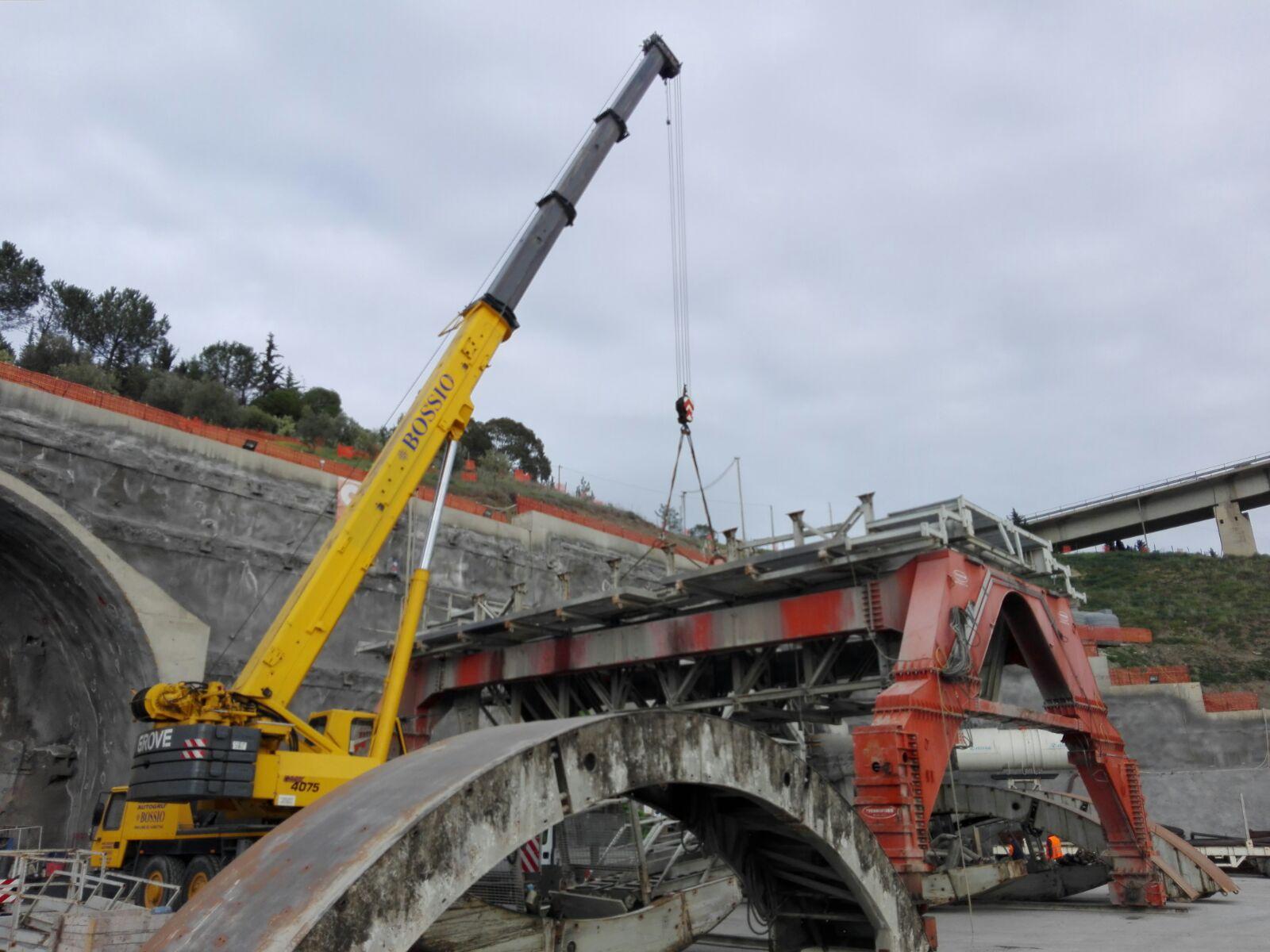Una gru gialla sta sollevando un pezzo di metallo sopra un ponte.