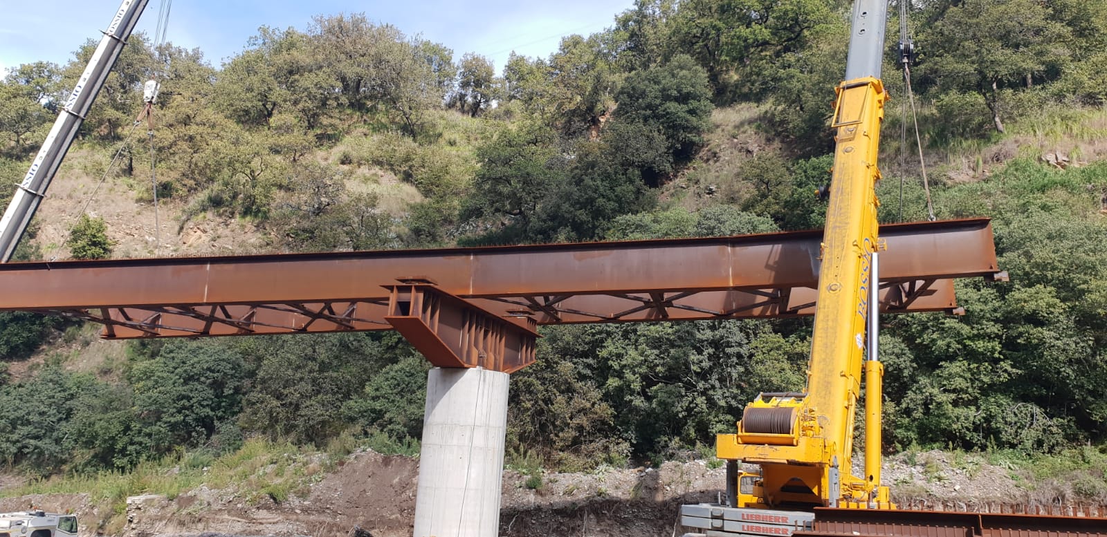 Una grande gru gialla sta sollevando un grande pezzo di metallo.