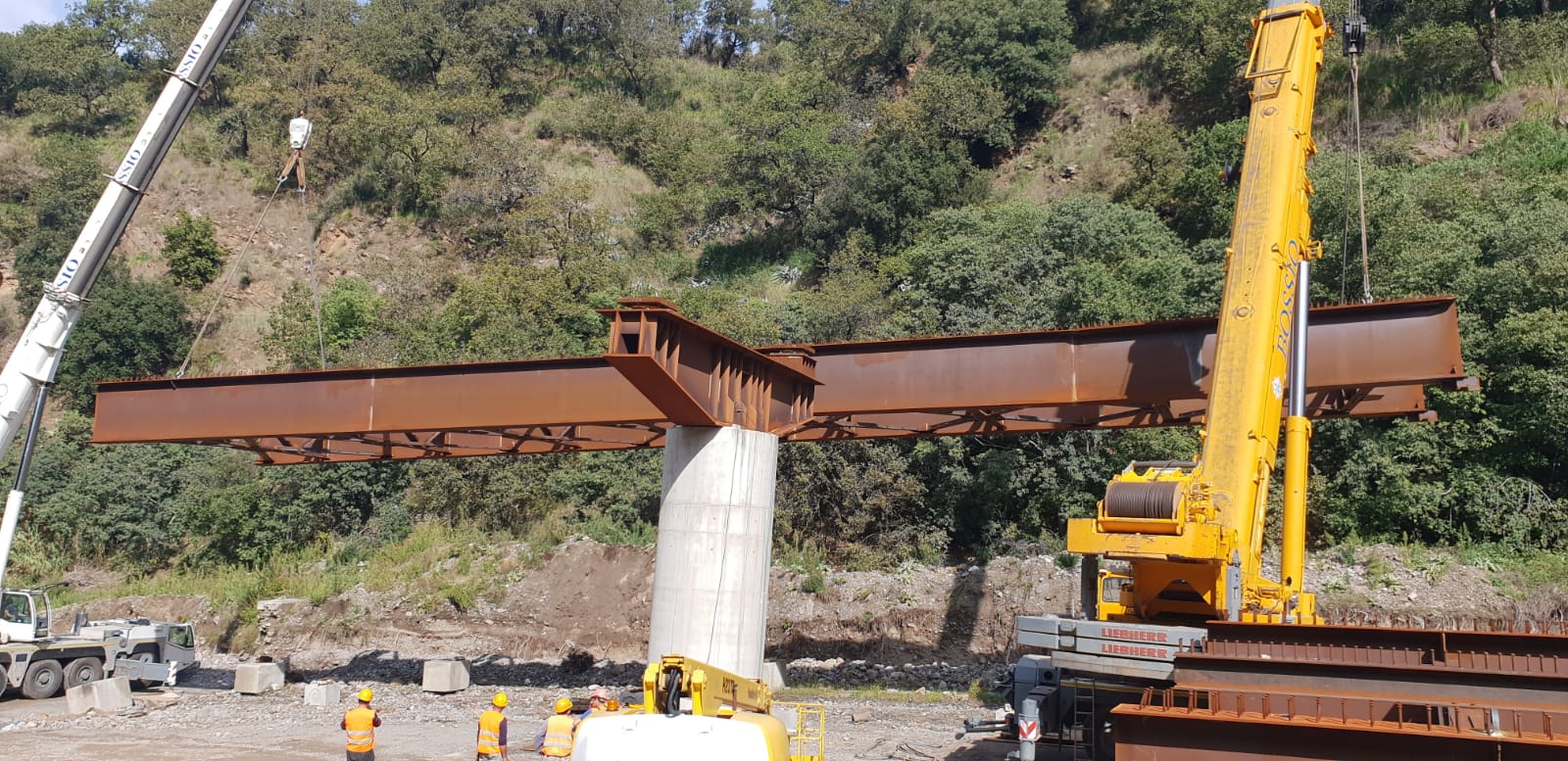 Una grande gru gialla sta sollevando un grande pezzo di metallo.