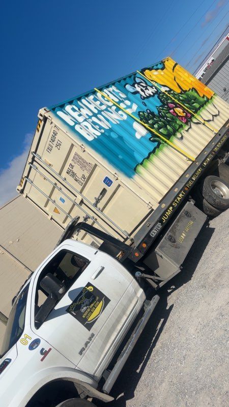 White truck carrying a beige graffiti-covered shipping container under a blue sky