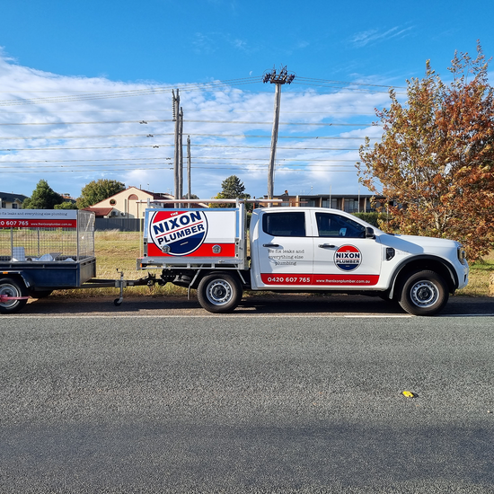 A white truck with a trailer attached to it is parked on the side of the road.