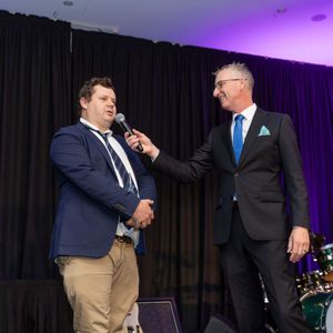 Two men in suits are talking into microphones on a stage