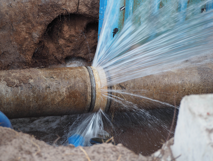 A pipe is leaking water in a hole in the ground.