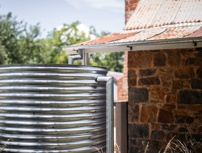 A metal water tank is sitting in front of a stone building.