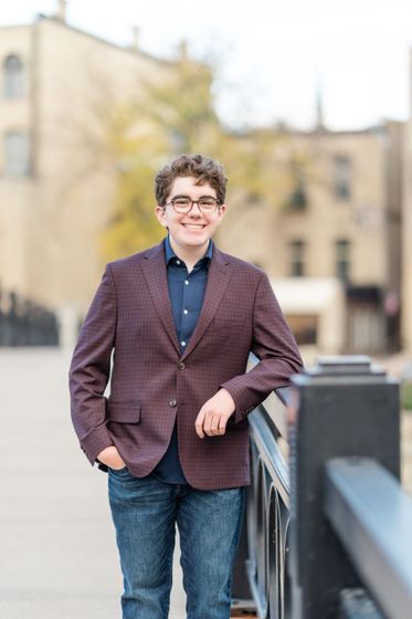 A young man in a suit and glasses is standing on a bridge.