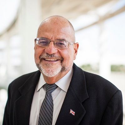 A man with glasses and a beard wearing a black suit and tie