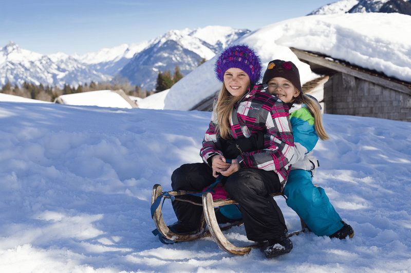Zwei junge Mädchen sitzen auf einem Schlitten im Schnee.