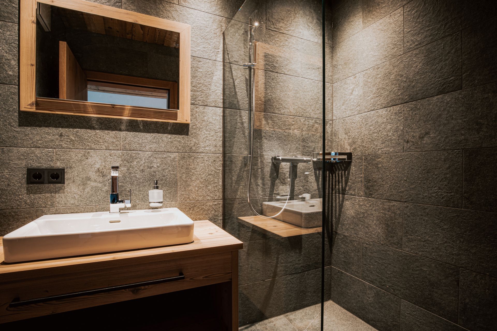 Ein Badezimmer mit Waschbecken, Spiegel und ebenerdiger Dusche.