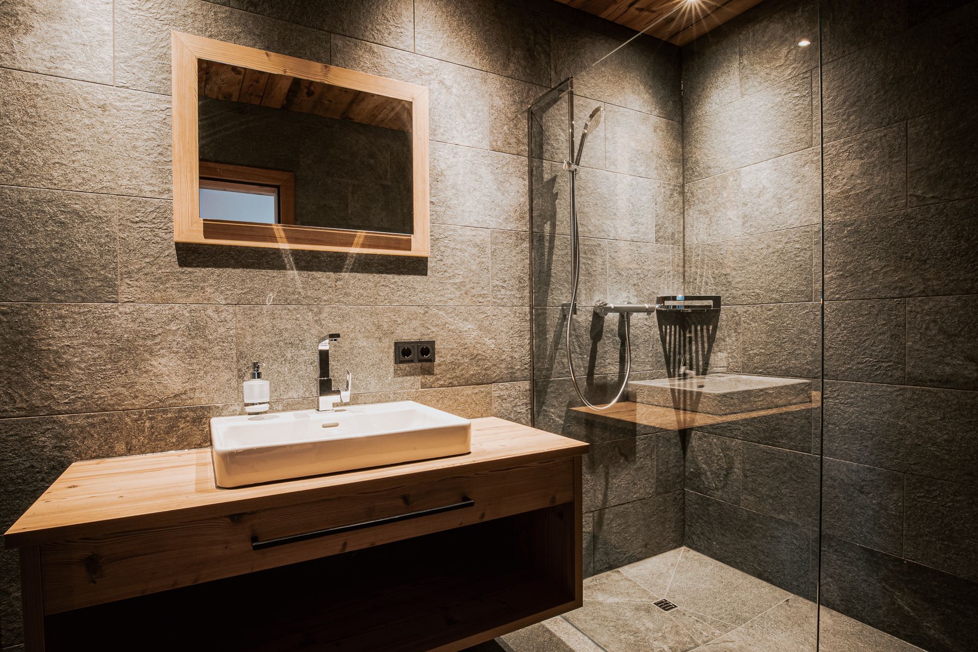 Ein Badezimmer mit Waschbecken, Spiegel und ebenerdiger Dusche.