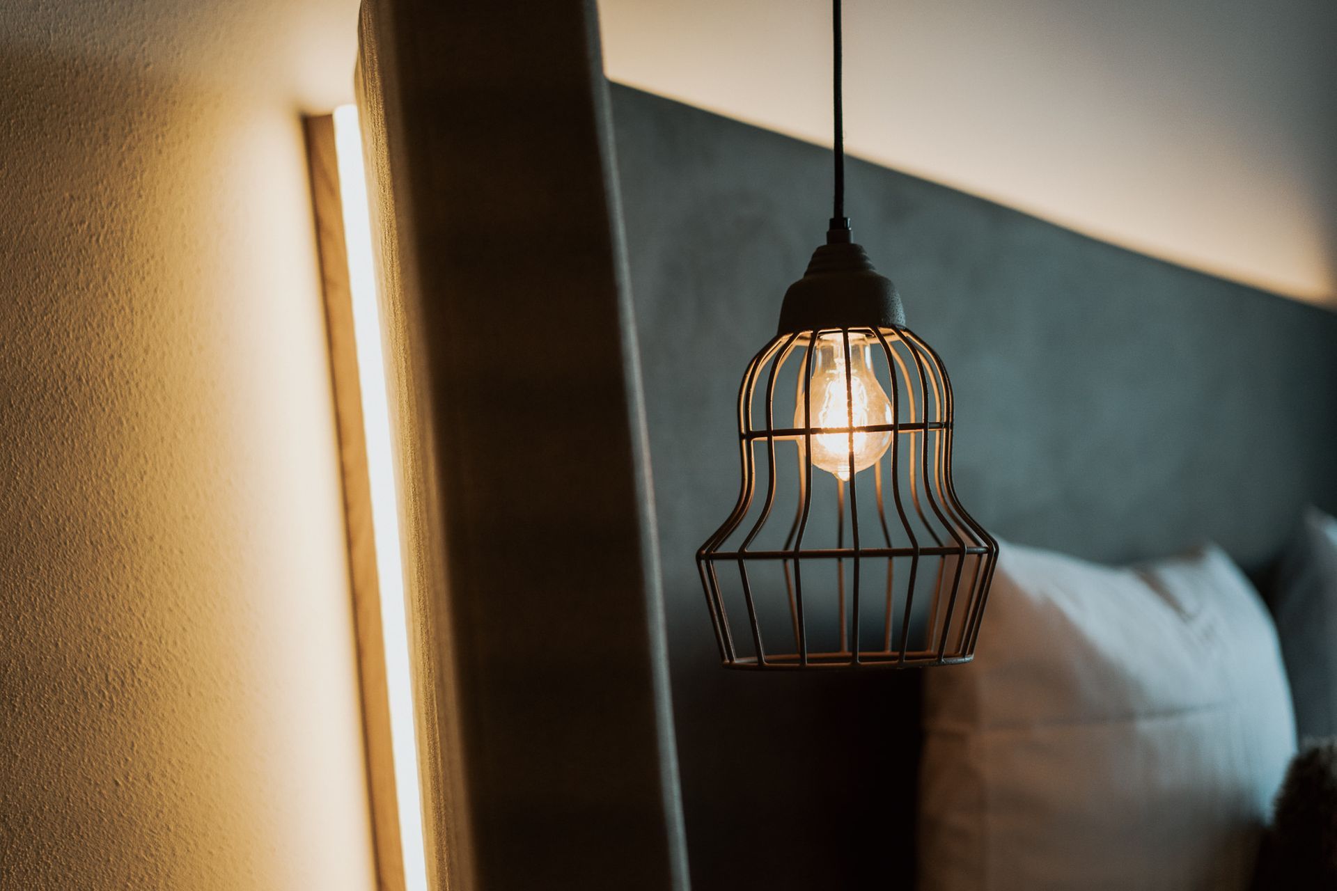 In einem Schlafzimmer hängt neben einem Bett eine Lampe von der Decke.