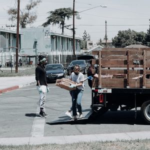 People unloading supplies from a truck in a residential area; some wearing masks and gloves.