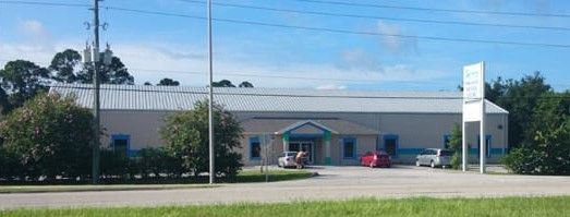 A low building with a metal roof and blue accents, a sign, and a red car parked outside.