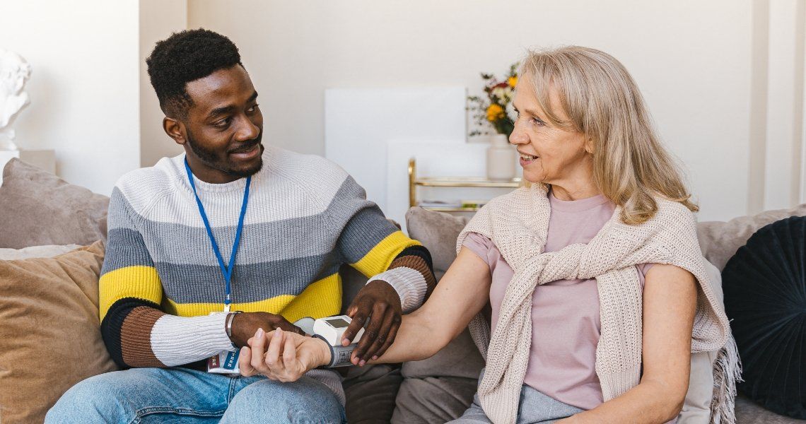 Man with badge comforts senior woman, smiling, indoors on a couch, holding her arm.