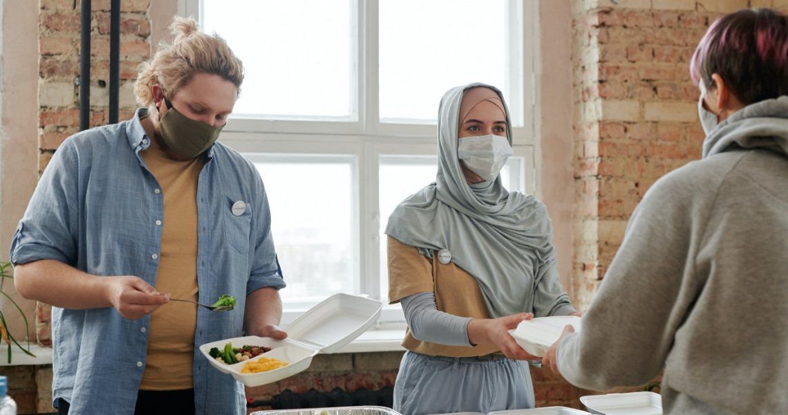 Volunteers wearing masks serving food from containers.