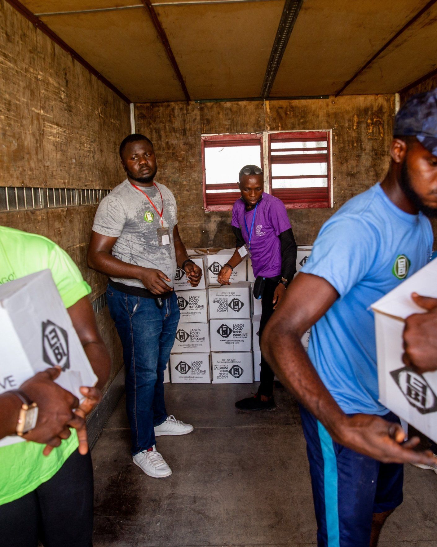 People loading boxes into a truck for delivery. Interior shot with boxes and workers wearing various colored shirts.