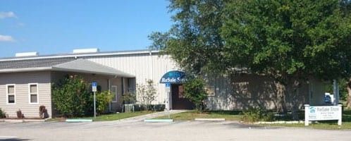 Exterior of a light-colored building with a blue arched entrance under a tree on a sunny day.
