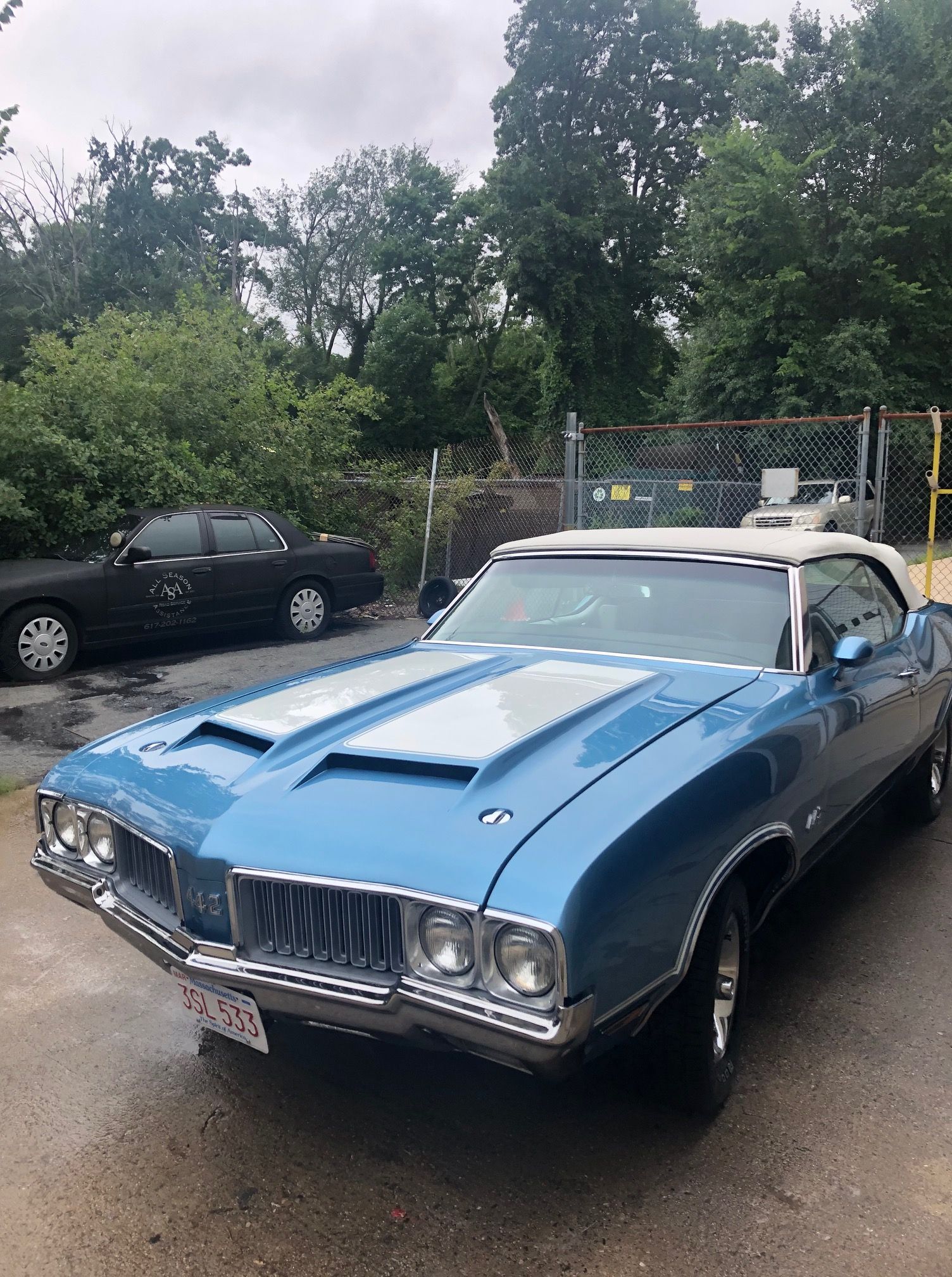 A blue oldsmobile cutlass supreme convertible is parked on the side of the road.