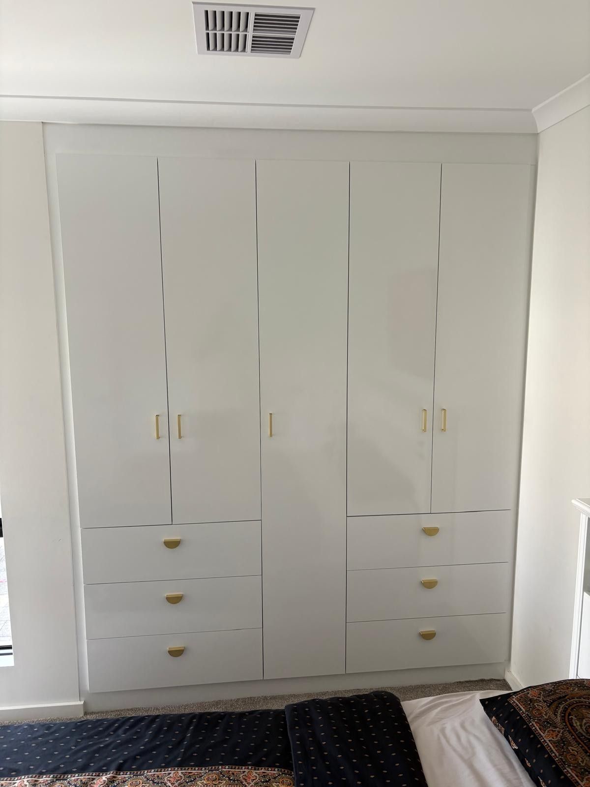 Modern hallway featuring a wall-mounted wood console, dark gray wardrobe cabinets, two white stools, and a potted plant.