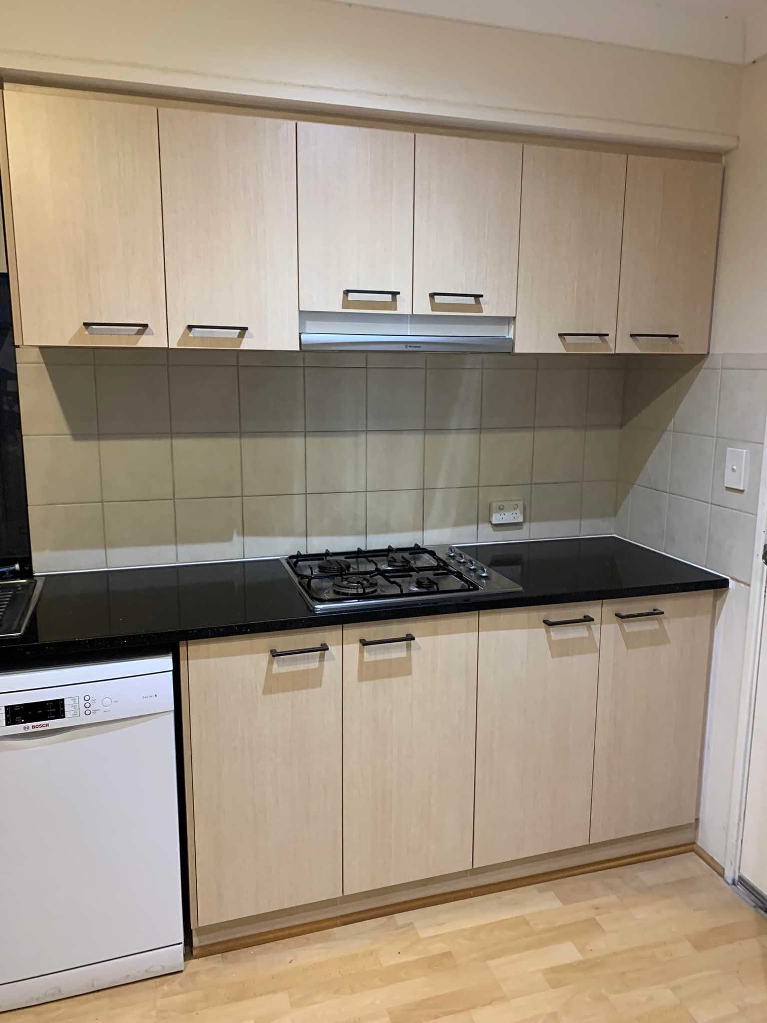 Light wood kitchen cabinets, black countertops, and a gas stove, with a dishwasher on the left.
