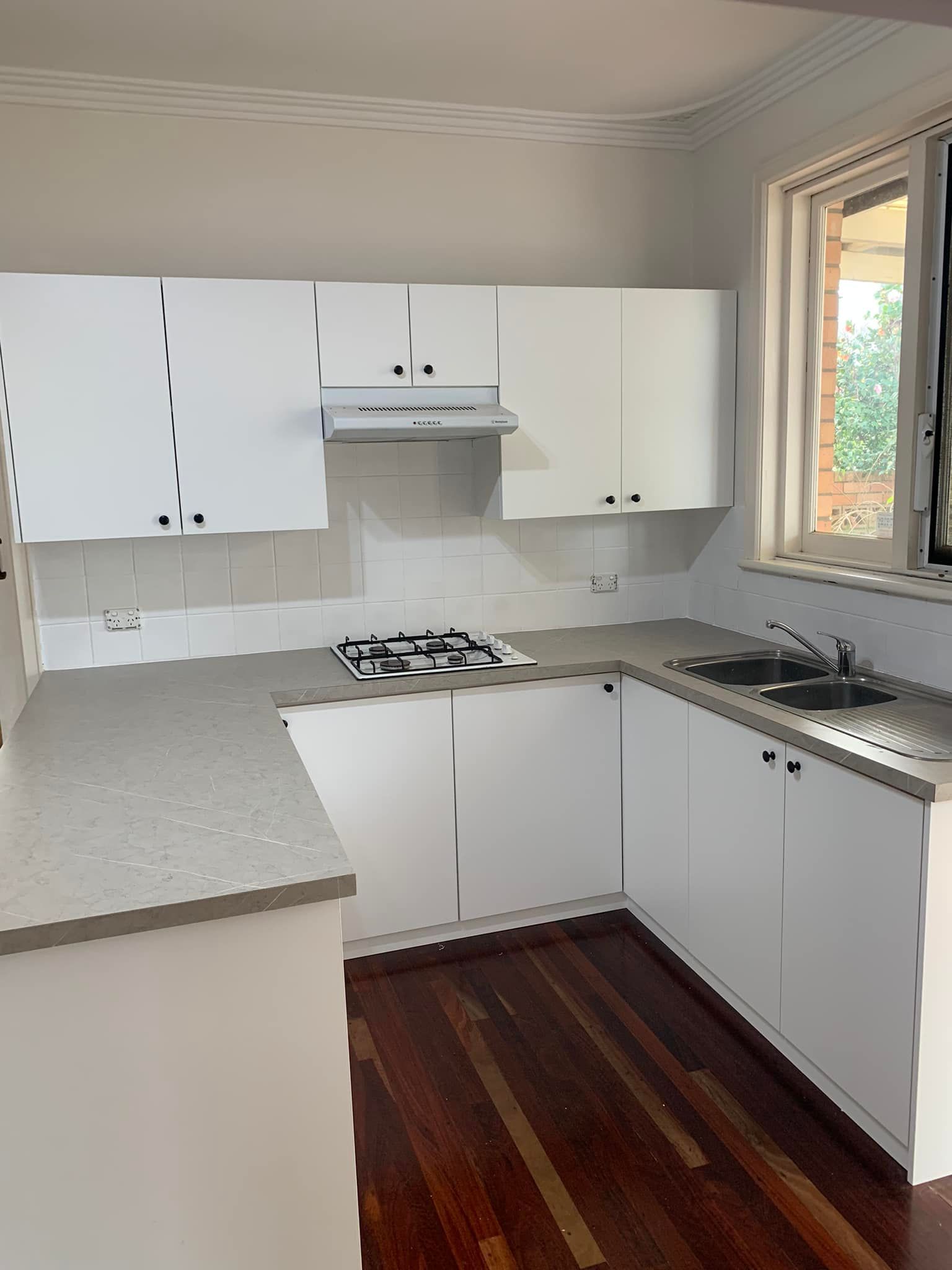 A kitchen featuring white cabinets, a light grey countertop, a gas stovetop, stainless steel sink, and dark wood floors.