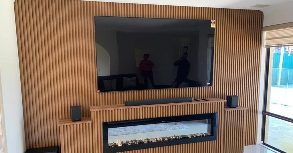 Large television mounted above an electric fireplace on a wall covered in vertical wooden slats.