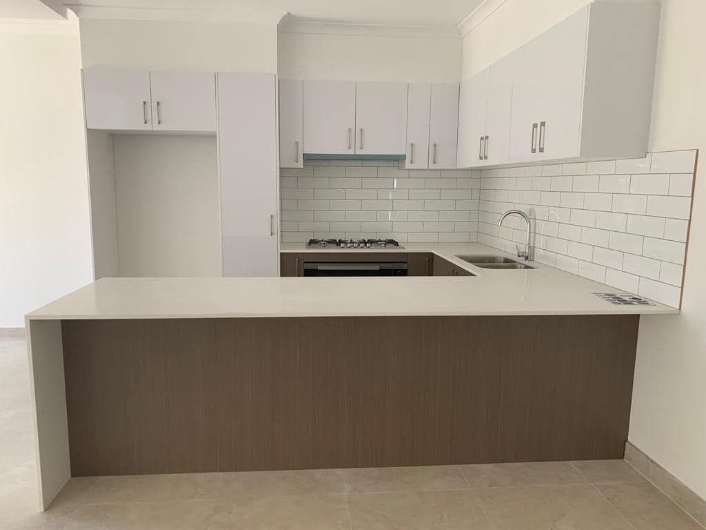 Modern kitchen with white upper cabinets, wood-tone base cabinets, white countertops, and white subway tile backsplash.