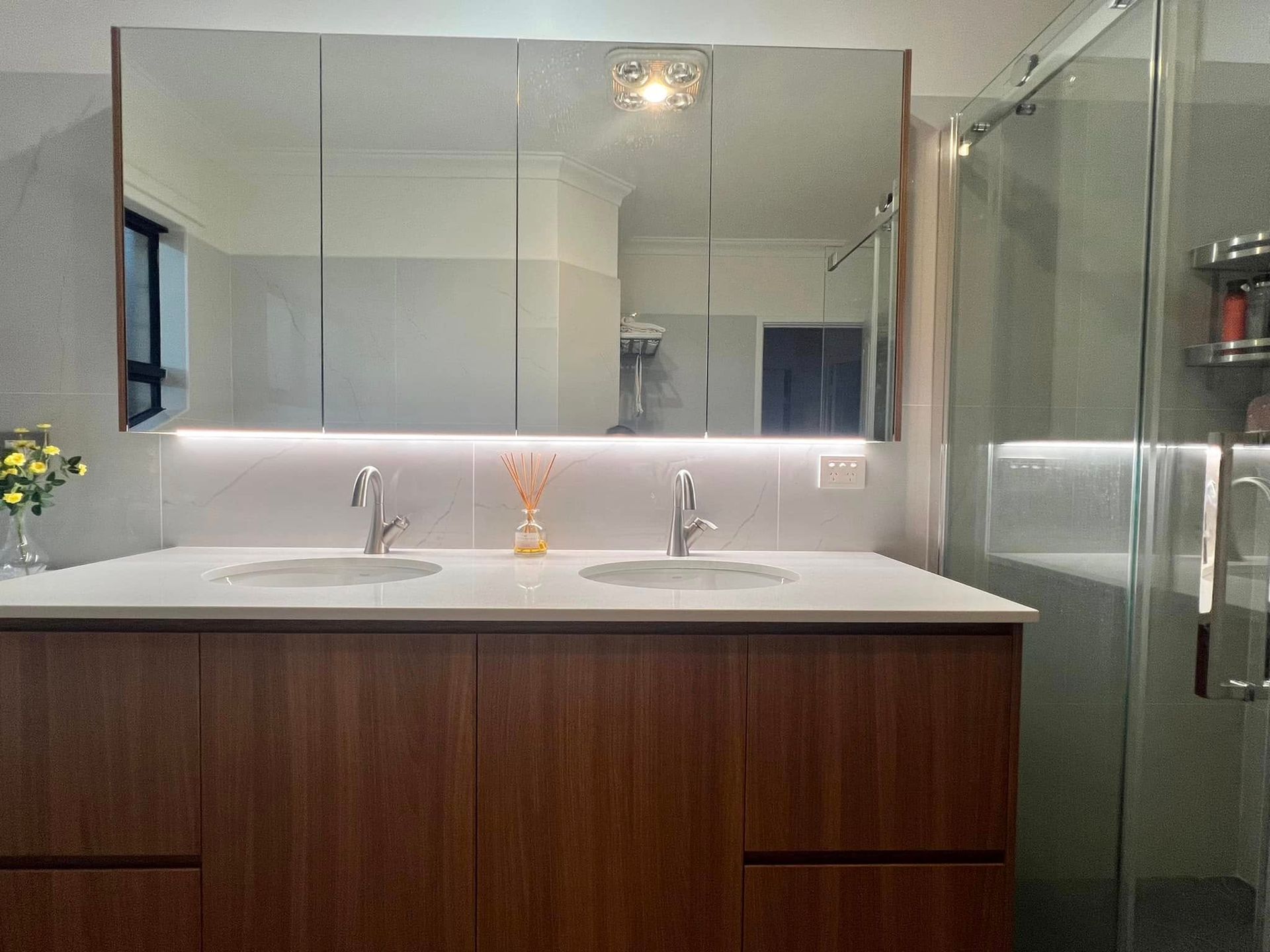 Double sink bathroom vanity with wooden cabinets, large mirrored medicine cabinets, and under-counter lighting.