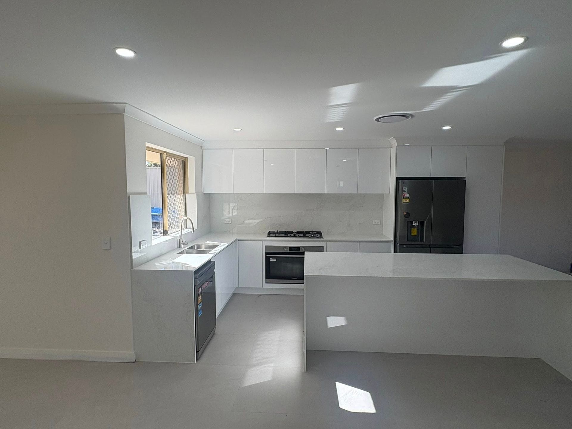Modern kitchen with white cabinets, light countertops, a kitchen island, and a black refrigerator.