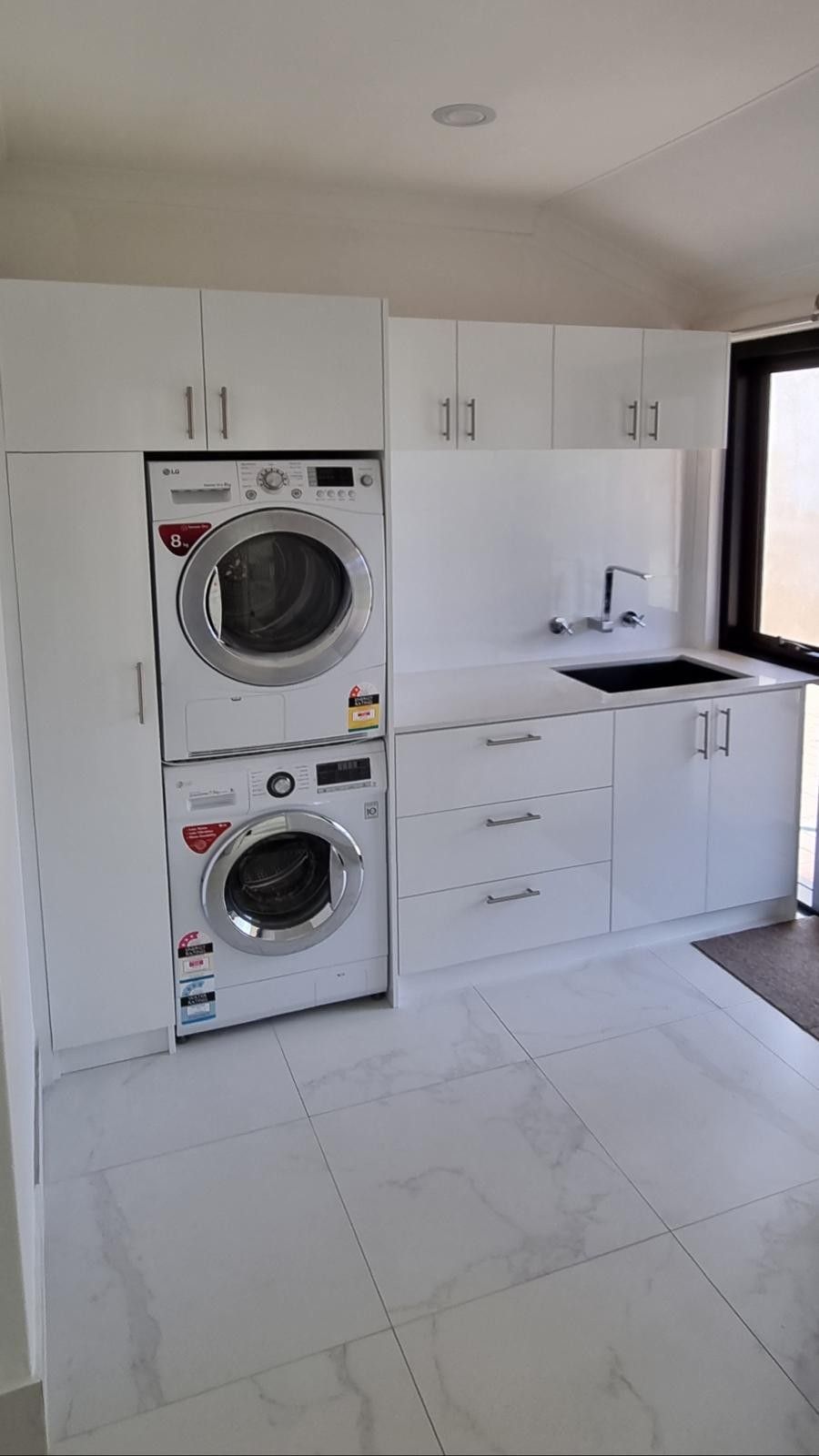 Laundry room with white cabinets, speckled granite counters, a sink, and two black washing machines on a wood floor.