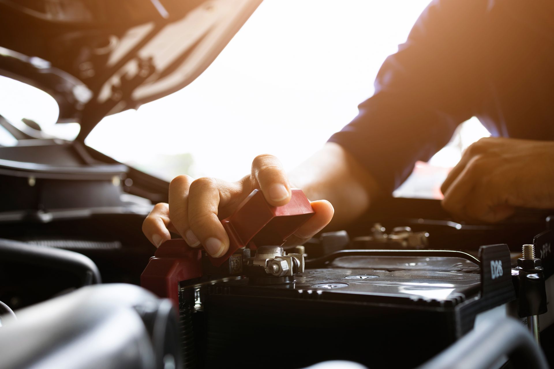 Person attaching a red battery clamp while working under the hood of a vehicle. Person attaching a red battery clamp while working under the hood of a vehicle.