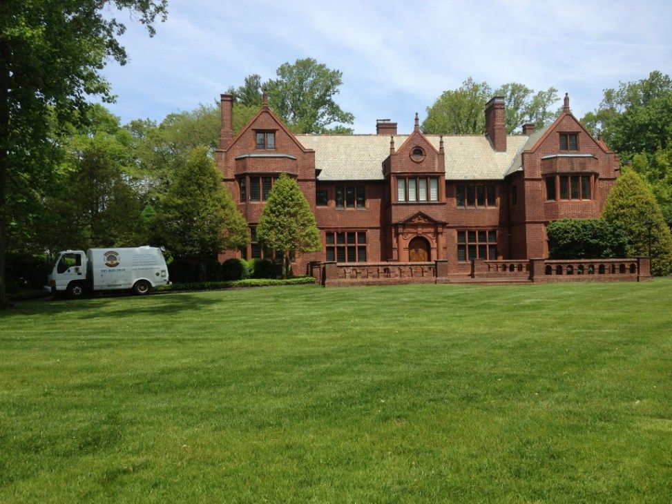 Red brick mansion with a white truck parked on the left side of a large green lawn.