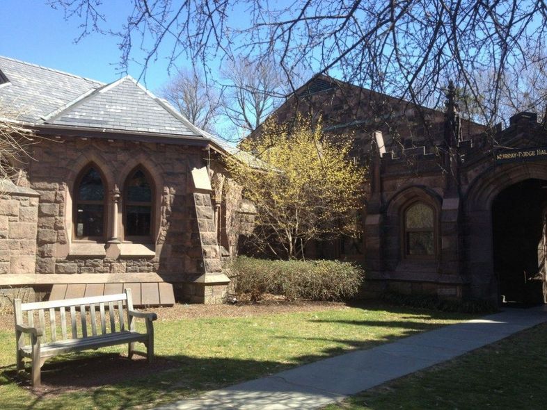 Stone buildings with arched windows and a bench on a green lawn.